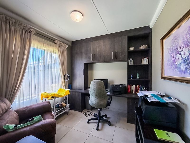 A functional home office featuring built-in dark wood cabinetry and desk space, tiled flooring, and natural light from a large window.
