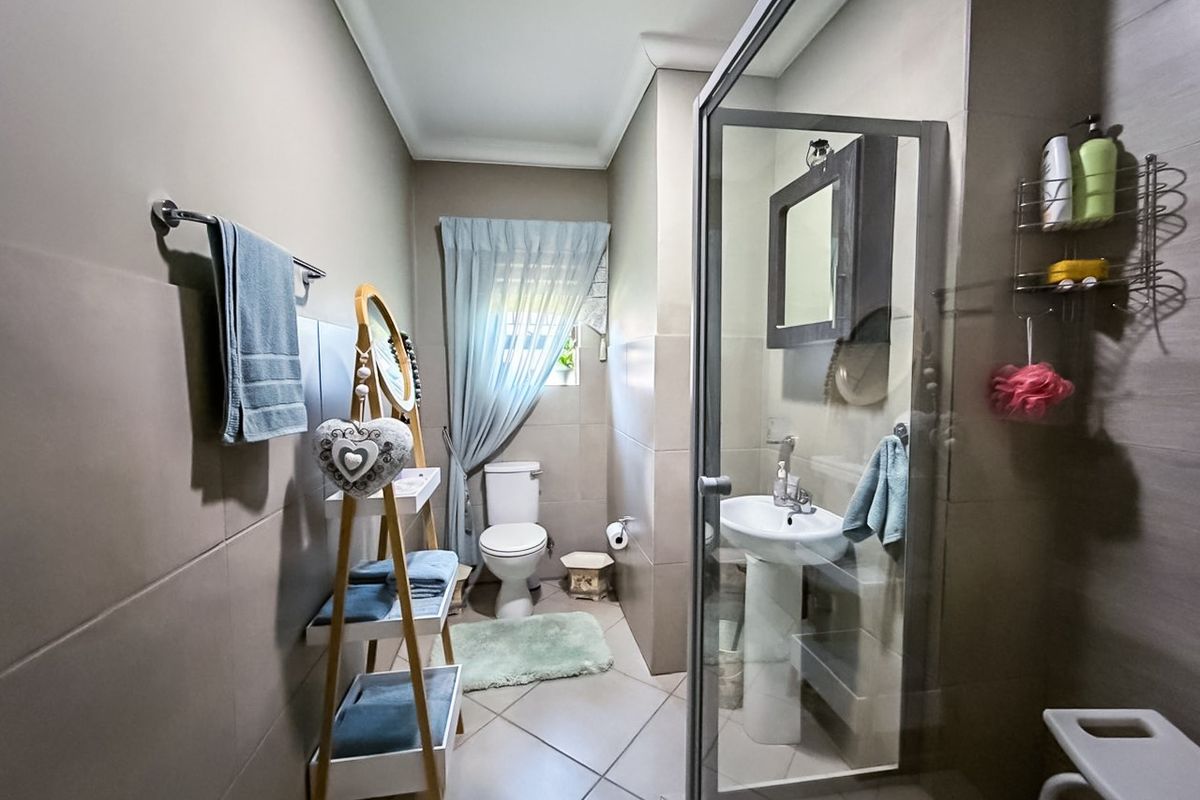 A functional bathroom featuring a pedestal basin, toilet, and a glass-enclosed shower with neutral wall and floor tiling.