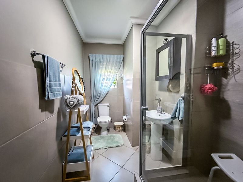 A functional bathroom featuring a pedestal basin, toilet, and a glass-enclosed shower with neutral wall and floor tiling.
