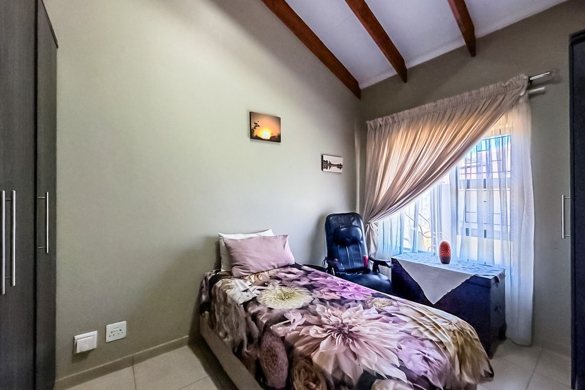 A cozy bedroom featuring exposed timber ceiling beams, tiled flooring, and a built-in wardrobe, offering a comfortable and functional living space.