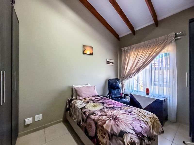 A cozy bedroom featuring exposed timber ceiling beams, tiled flooring, and a built-in wardrobe, offering a comfortable and functional living space.