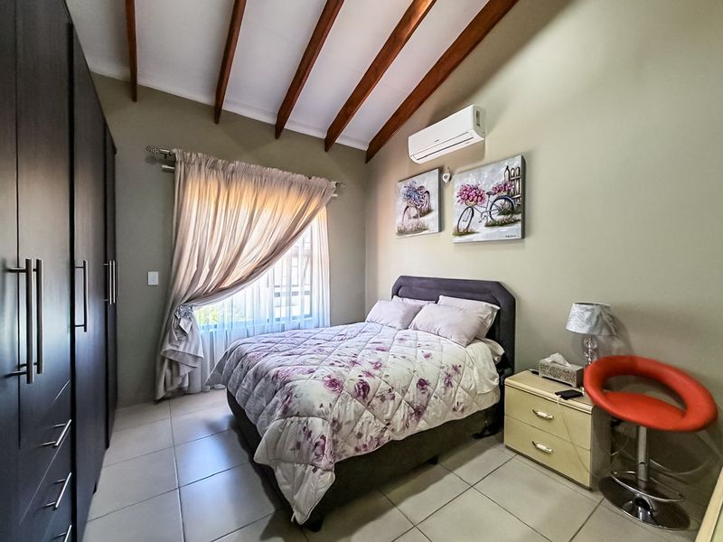 A well-maintained bedroom featuring exposed timber ceiling beams, tiled flooring, a built-in wardrobe, and a wall-mounted air conditioning unit.