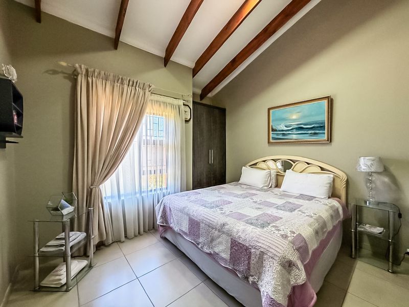 A well-maintained bedroom featuring high vaulted ceilings with exposed timber beams, tiled flooring, and a built-in wardrobe.