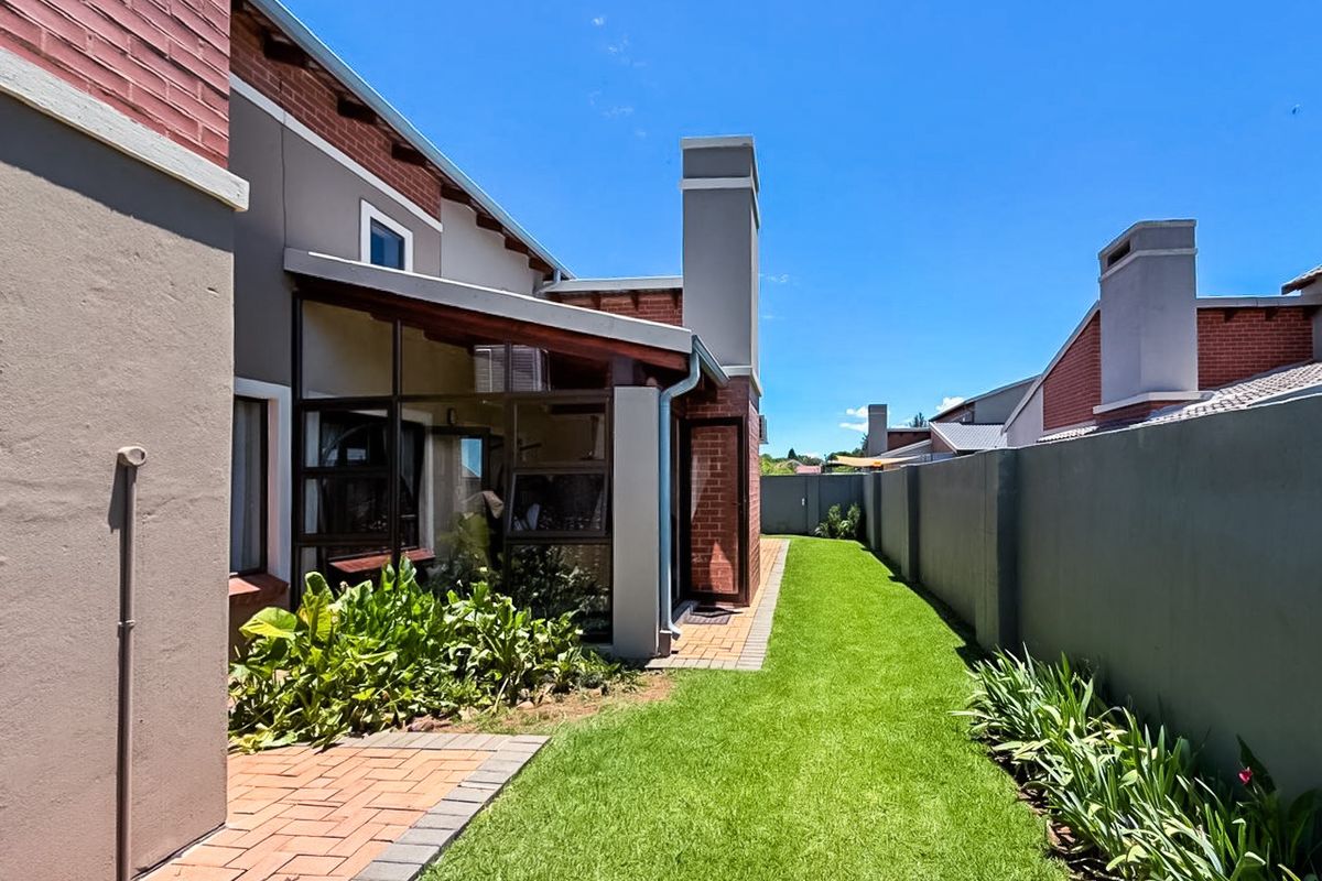 Rear view of the townhouse featuring a well-maintained lawn, paved patio area, and an enclosed patio structure with a brick chimney.