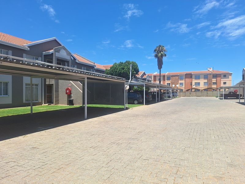 Exterior view of an apartment complex featuring covered parking bays and a paved driveway area.