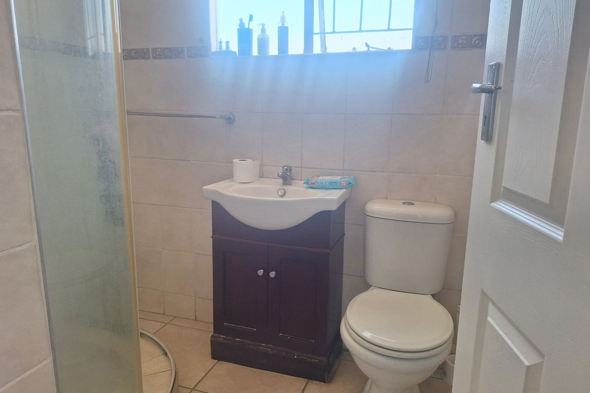 A functional bathroom featuring a vanity cabinet, toilet, and shower enclosure with tiled finishes throughout.