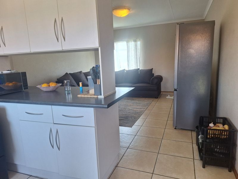Open plan kitchen and living area featuring neutral cabinetry, dark countertops, and ceramic floor tiles throughout the connected space.