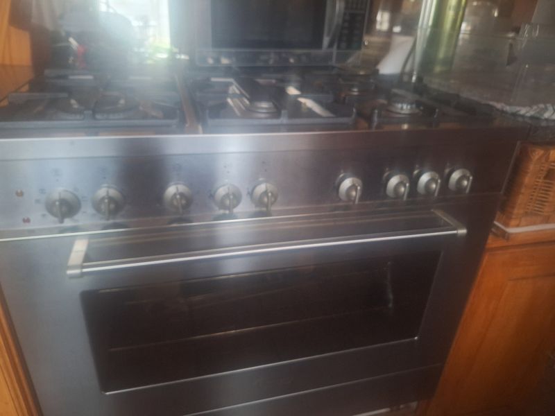 A stainless steel freestanding gas stove and oven unit integrated into wooden kitchen cabinetry with an overhead built-in microwave.