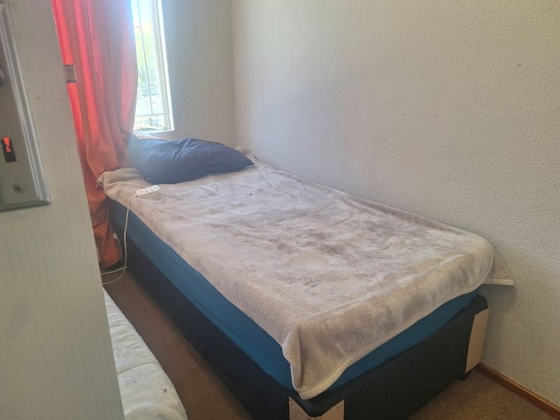 A compact bedroom featuring a single window with security bars and textured wall finishes.