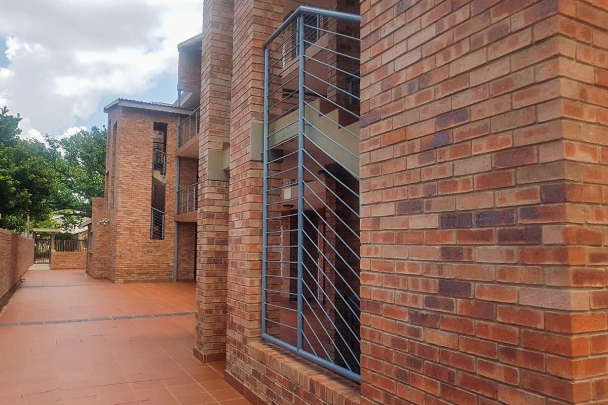 Exterior view of an apartment complex featuring face brick architecture, metal balustrades, and a paved walkway.