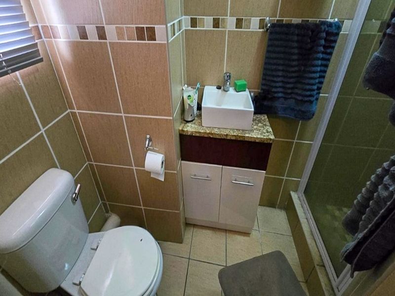 Compact bathroom featuring a vessel sink with vanity cabinet, a standard toilet, and a glass-enclosed shower with neutral wall and floor tiling.