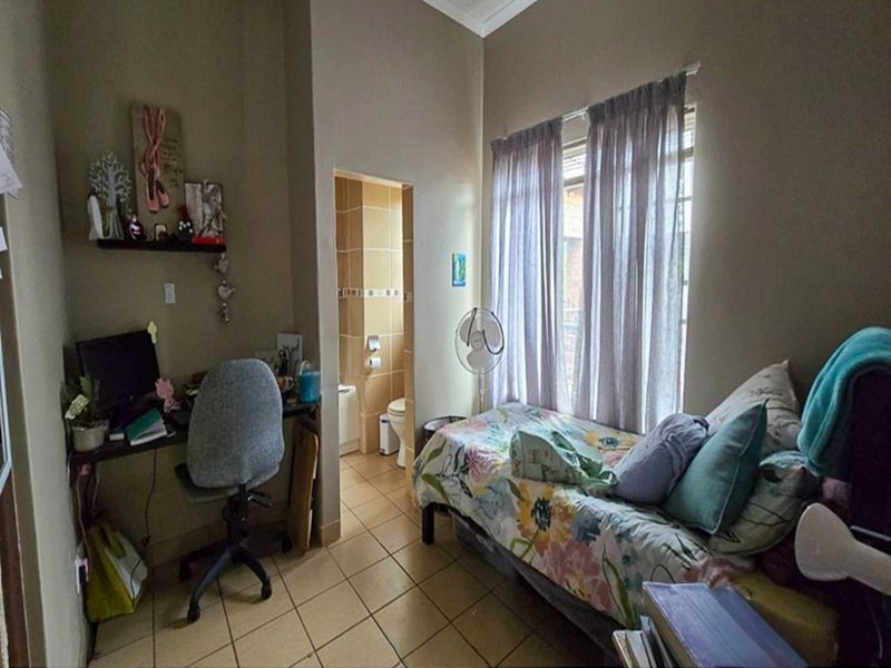 A bedroom featuring tiled flooring and an attached en-suite bathroom, providing a functional living space with natural light from the window.