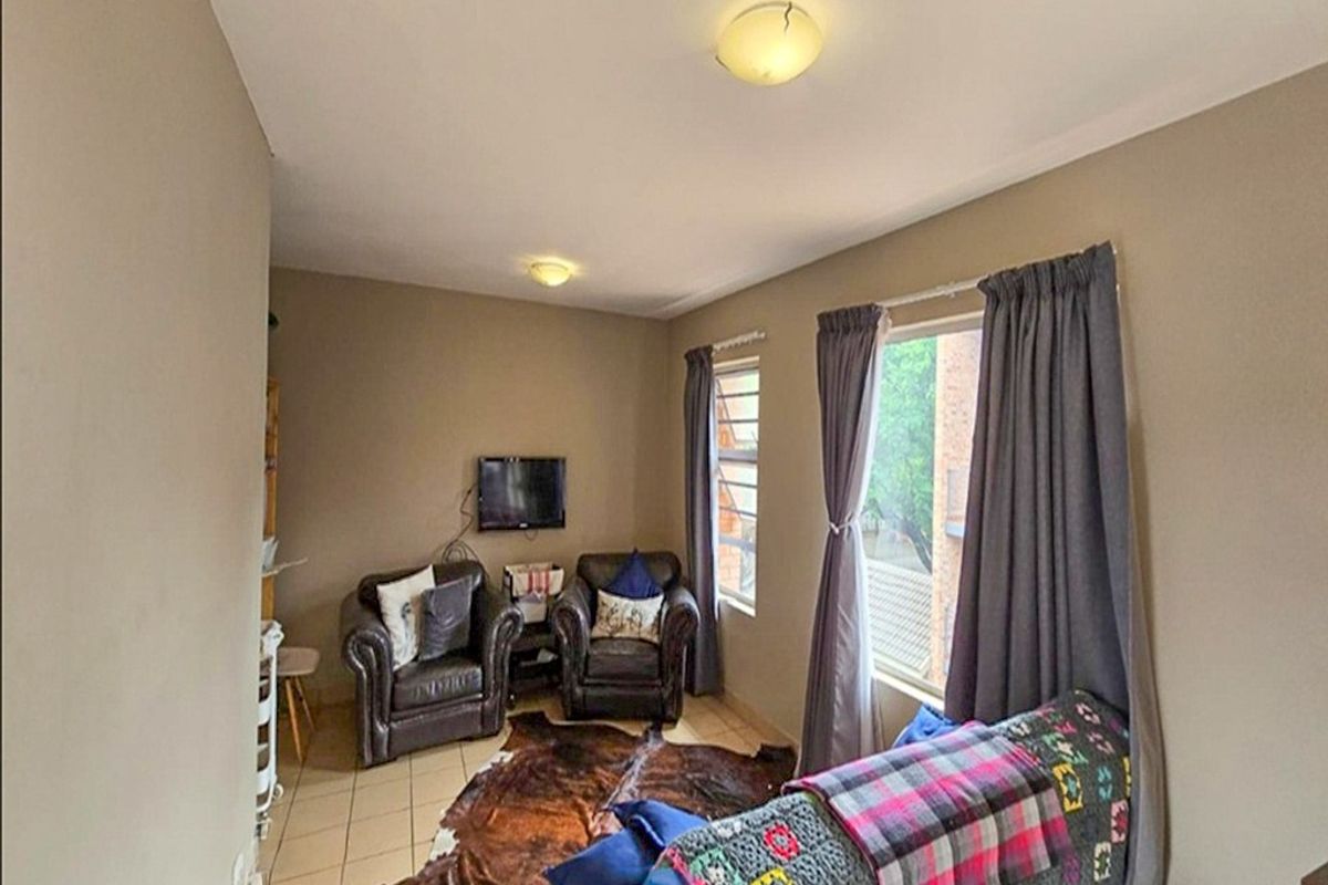 A functional living room featuring tiled flooring and natural light from dual windows, providing a comfortable space for relaxation.