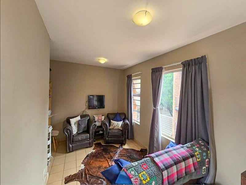 A functional living room featuring tiled flooring and natural light from dual windows, providing a comfortable space for relaxation.
