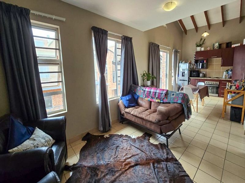 Open-plan living and kitchen area featuring tiled floors, vaulted ceilings with exposed timber beams, and functional kitchen cabinetry with built-in appliances.