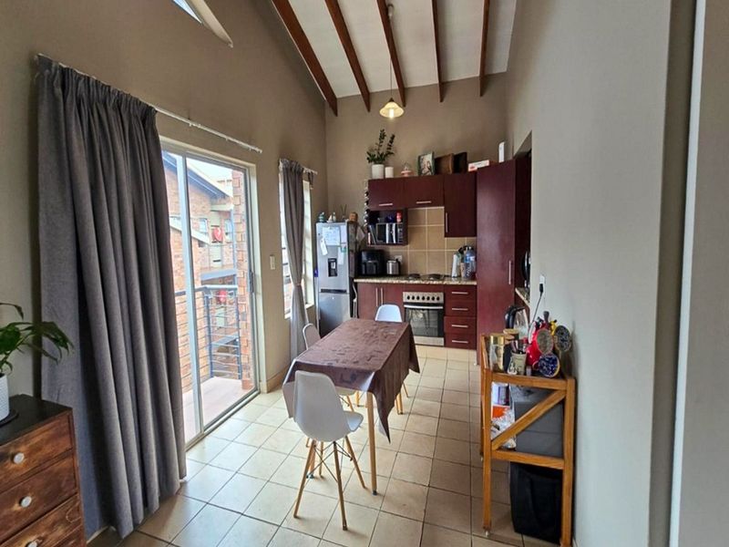 Open-plan kitchen and dining area featuring vaulted ceilings with exposed timber beams, tiled flooring, and a sliding door leading to a balcony.