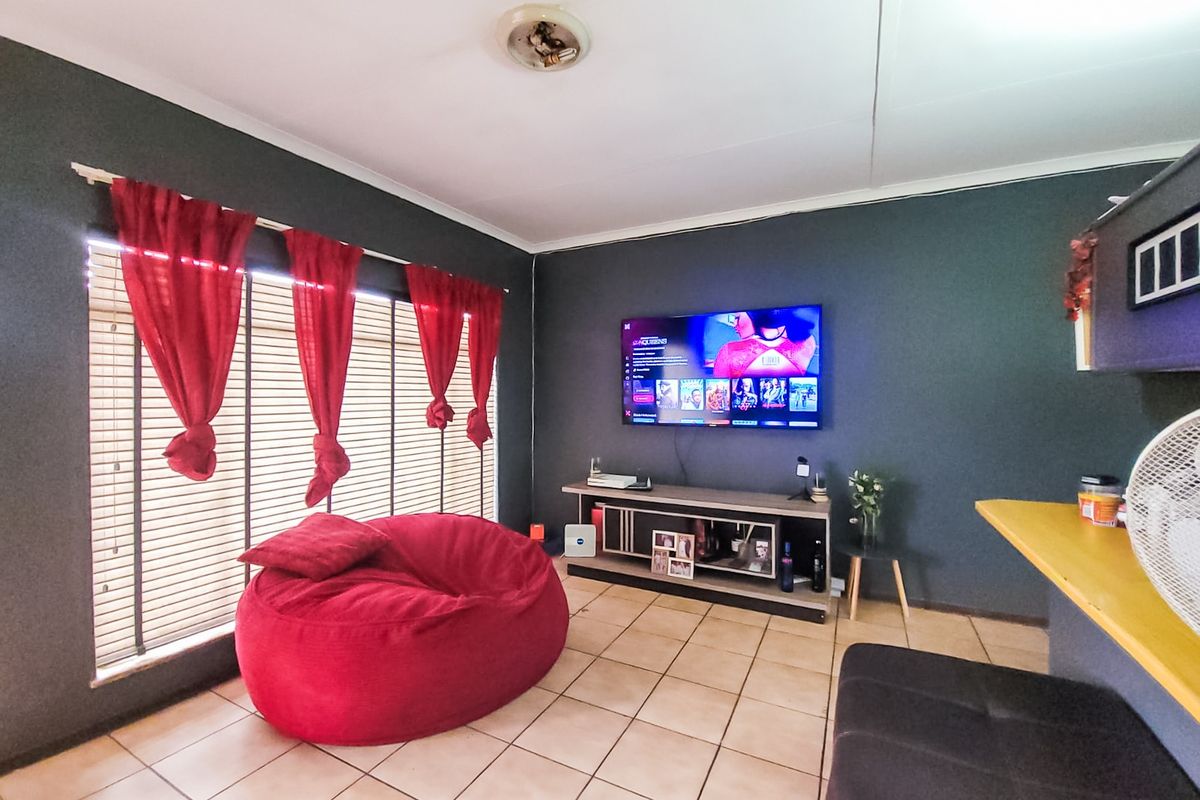 A living room featuring tiled flooring, venetian blinds, and a wall-mounted television, providing a functional space for relaxation.