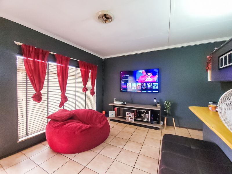 A living room featuring tiled flooring, venetian blinds, and a wall-mounted television, providing a functional space for relaxation.