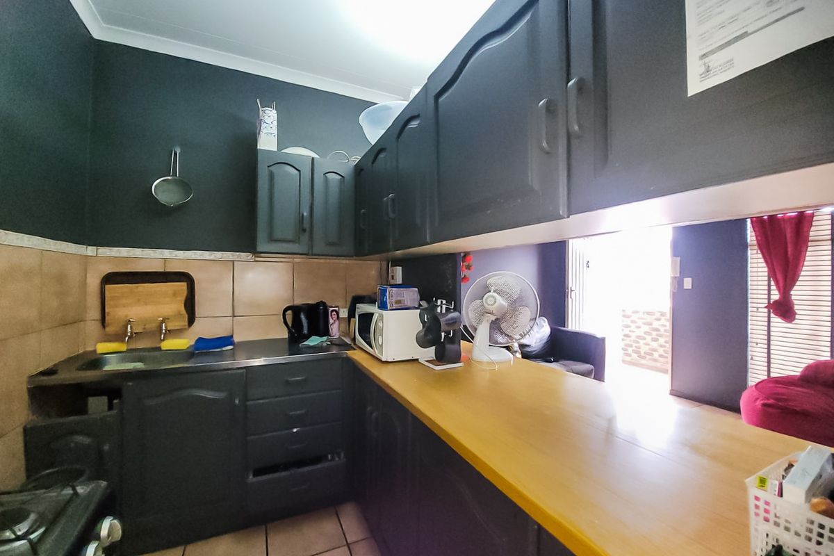 A compact kitchen featuring dark cabinetry, a wooden countertop, tiled backsplash, and a gas stove, with an open layout leading to the living area.