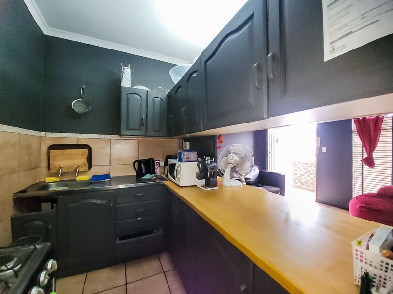 A compact kitchen featuring dark cabinetry, a wooden countertop, tiled backsplash, and a gas stove, with an open layout leading to the living area.