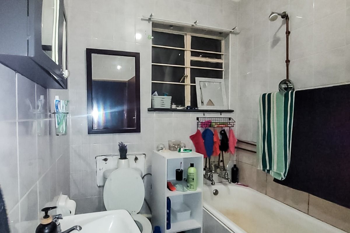 A functional bathroom featuring a pedestal basin, toilet, and a bathtub with a shower head, finished with wall tiles throughout.
