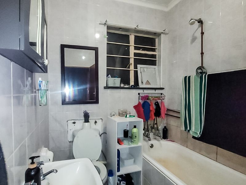 A functional bathroom featuring a pedestal basin, toilet, and a bathtub with a shower head, finished with wall tiles throughout.