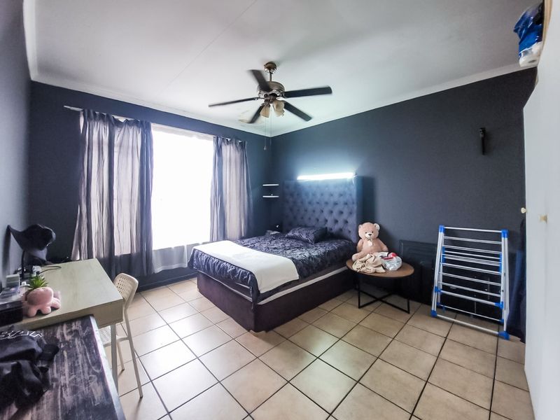 Spacious bedroom featuring tiled flooring, a ceiling fan, and a built-in headboard with integrated lighting.