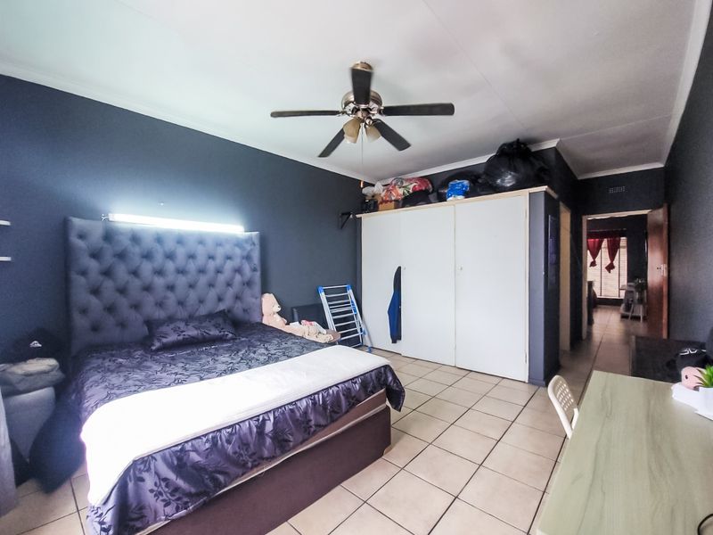 A bedroom featuring tiled flooring, a ceiling fan, and built-in cupboards, with dark accent walls providing a modern aesthetic.