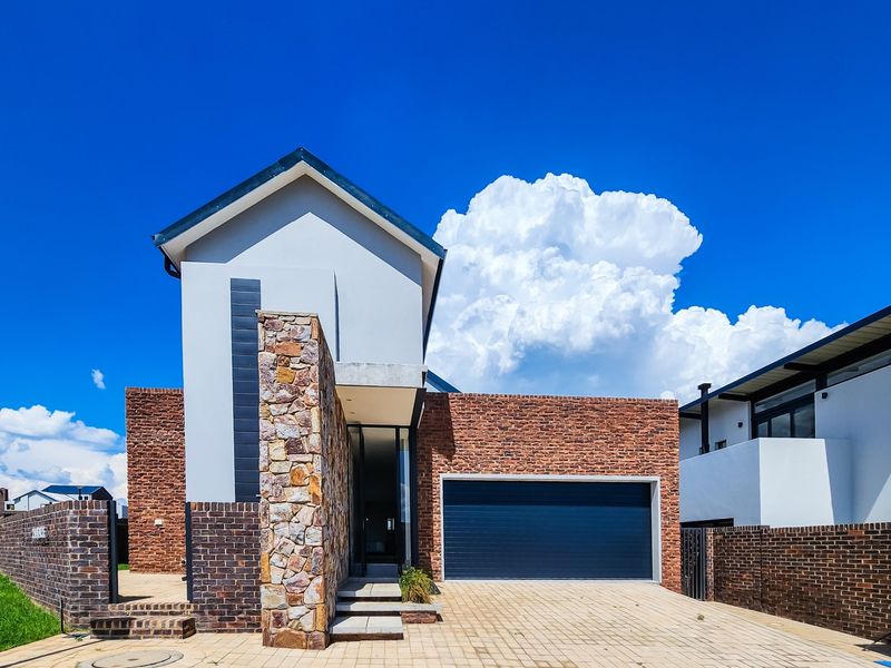 Modern architectural house exterior featuring a combination of face brick and stone cladding, with a paved driveway and integrated double garage.