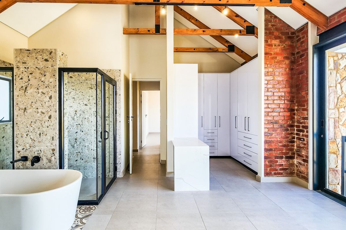 Spacious modern bathroom featuring a freestanding tub, walk-in shower, exposed timber beams, brick feature wall, and ample built-in storage cabinetry.