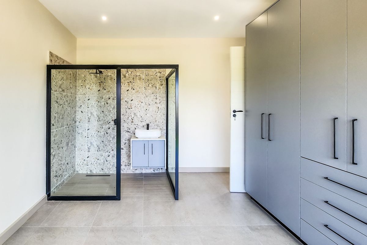 Modern bedroom featuring an open-plan ensuite shower area with terrazzo tiling, a sleek wall-mounted vanity, and extensive built-in grey cabinetry.