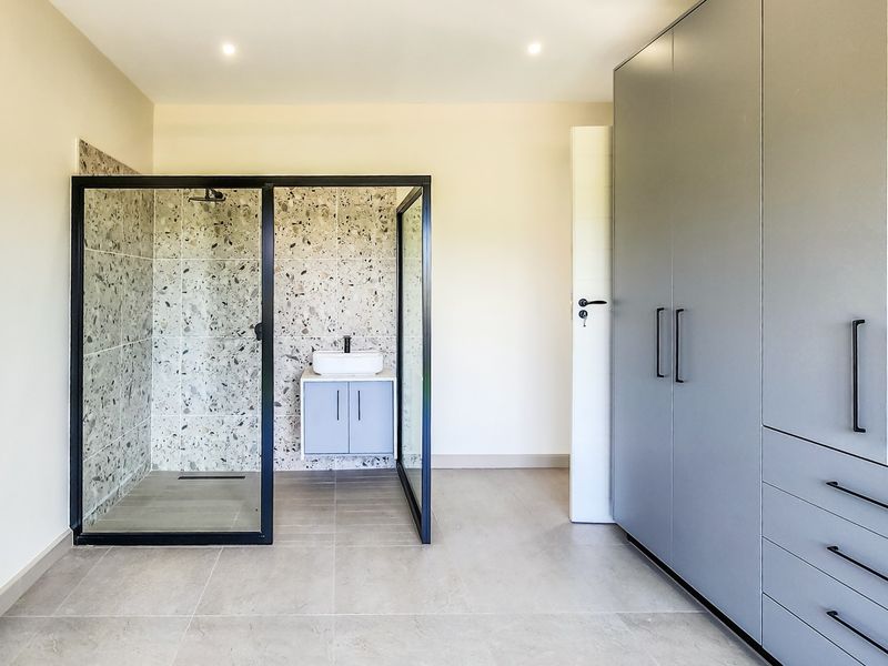 Modern bedroom featuring an open-plan ensuite shower area with terrazzo tiling, a sleek wall-mounted vanity, and extensive built-in grey cabinetry.
