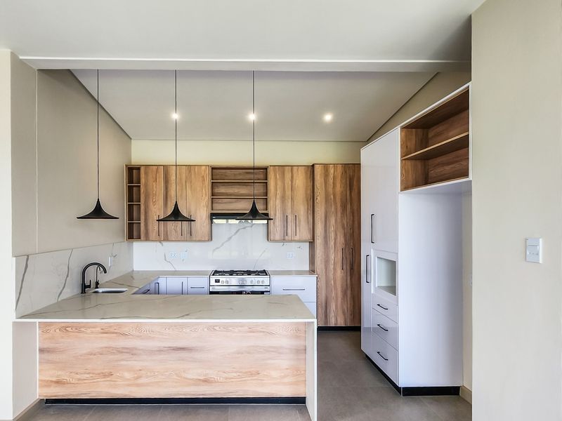 Modern kitchen featuring wood-grain cabinetry, stone countertops, integrated gas cooktop, and stylish pendant lighting in a clean, contemporary layout.
