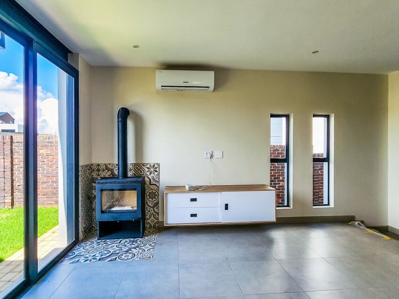Modern open-plan living area featuring a sleek freestanding fireplace, tiled floors, split-system air conditioning, and large sliding doors opening to the garden.