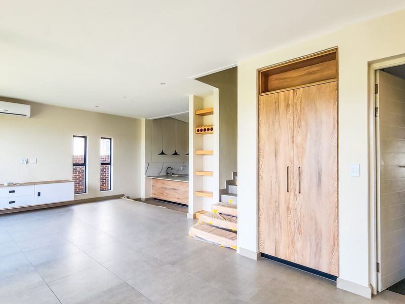 Spacious open-plan living area featuring a wood-burning fireplace, modern tiled flooring, built-in storage, and a sleek kitchen with integrated cabinetry.