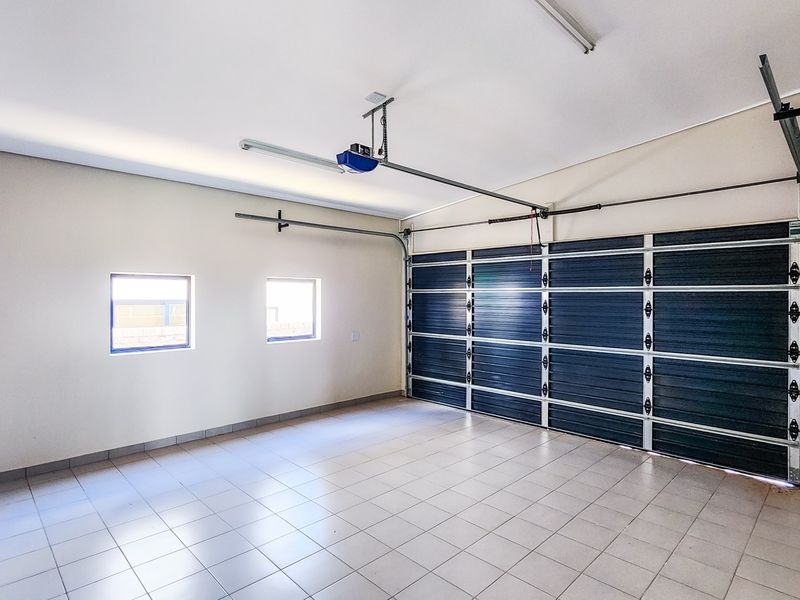 A clean, spacious double garage featuring tiled flooring, automated door mechanism, and neutral wall finishes, providing ample secure parking and storage space.