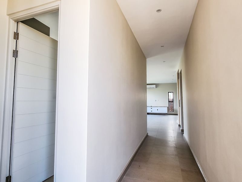 A clean, neutral hallway featuring tiled flooring and recessed lighting, providing a seamless transition between the home's living spaces.