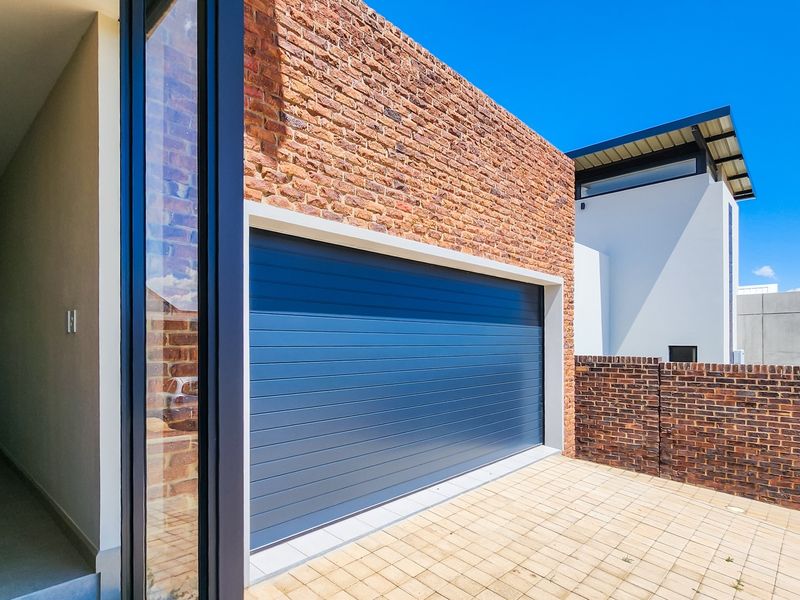 Modern exterior view featuring a brick facade, a blue sectional garage door, and a paved driveway area.