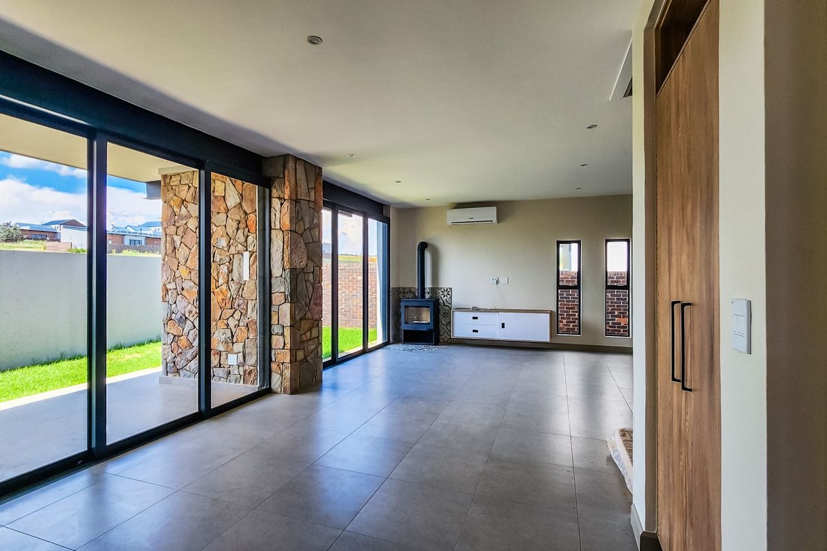 Spacious open-plan living area featuring large sliding glass doors, a stone feature wall, a wood-burning fireplace, and modern tiled flooring.