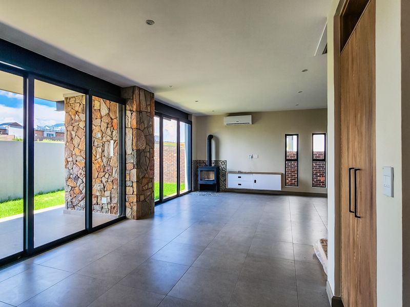 Spacious open-plan living area featuring large sliding glass doors, a stone feature wall, a wood-burning fireplace, and modern tiled flooring.