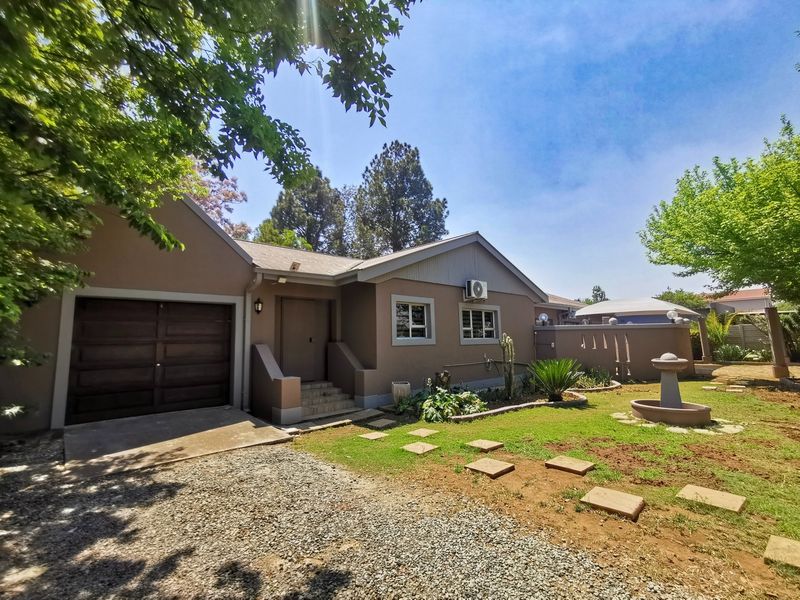 Front view of the property featuring a single garage, paved driveway, landscaped garden with a stone fountain, and exterior wall-mounted air conditioning unit.