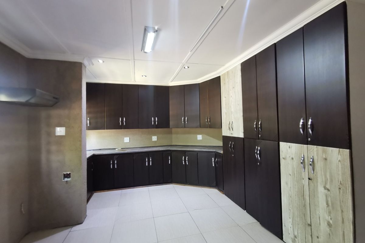A spacious, empty kitchen featuring dark built-in cabinetry, light-toned accent panels, tiled flooring, and integrated extractor fan, offering a clean canvas for customization.