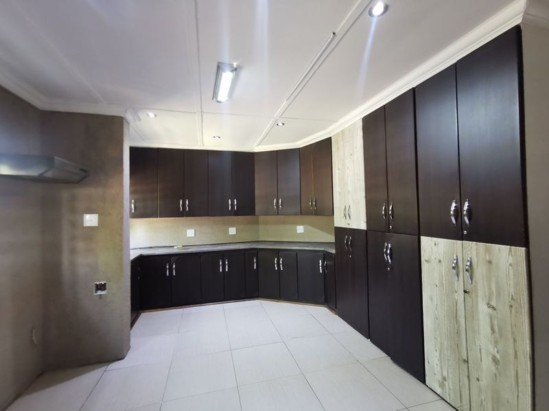 A spacious, empty kitchen featuring dark built-in cabinetry, light-toned accent panels, tiled flooring, and integrated extractor fan, offering a clean canvas for customization.