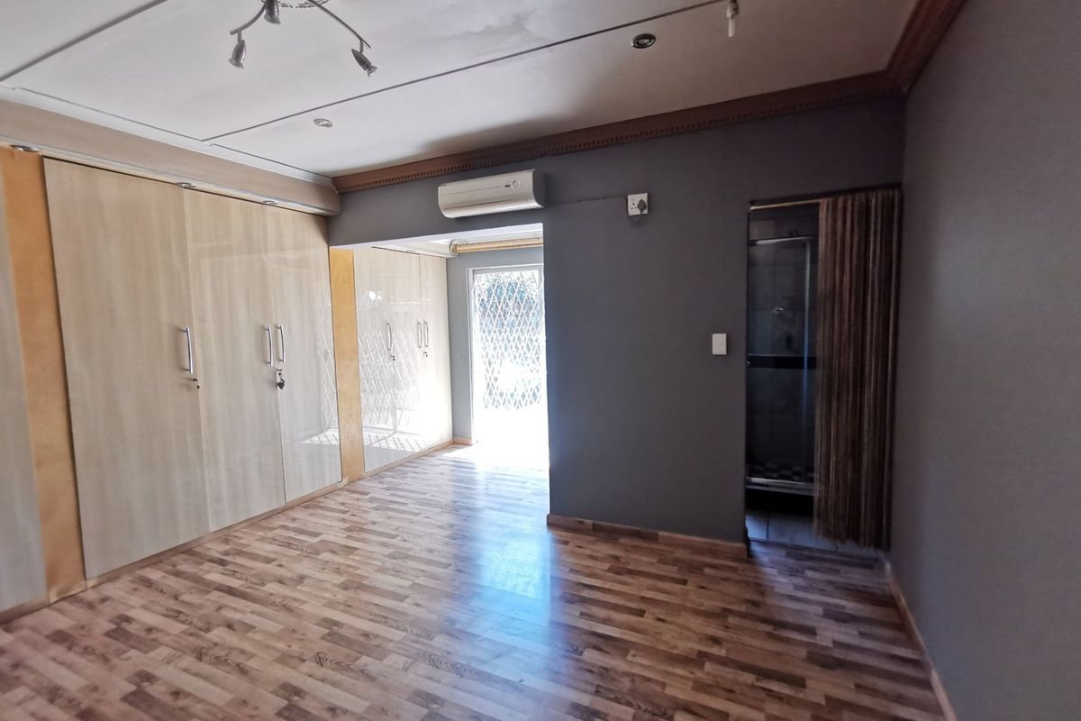 Spacious bedroom featuring extensive built-in cupboards, laminate flooring, an air conditioning unit, and direct access to an en-suite bathroom.