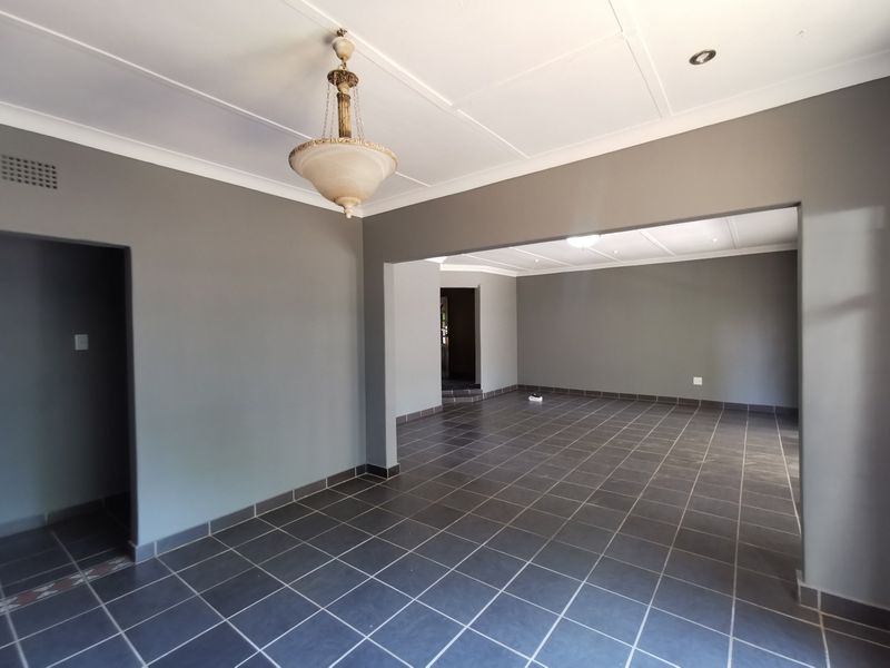 Spacious open-plan living area featuring neutral grey walls, dark tiled flooring, and a combination of pendant and recessed ceiling lighting.
