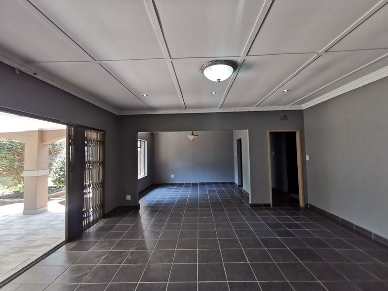 Spacious, empty living area featuring dark tiled flooring, a suspended ceiling with recessed lighting, and a sliding door leading to an outdoor patio.