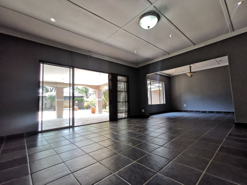 Spacious, empty living area featuring dark tiled flooring, recessed ceiling lights, and large sliding doors providing direct access to the outdoor patio.