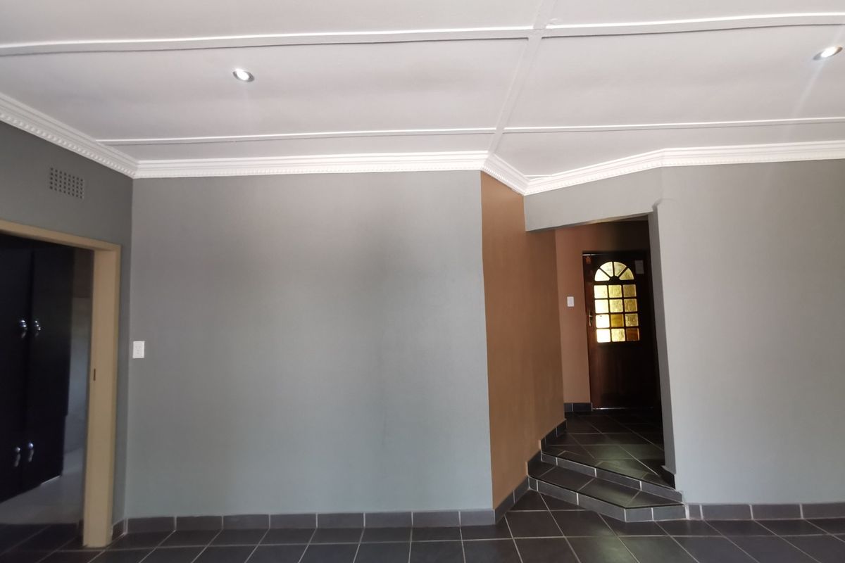 An empty living area featuring dark tiled flooring, recessed downlighting, and a coved ceiling, leading to a timber entrance door.