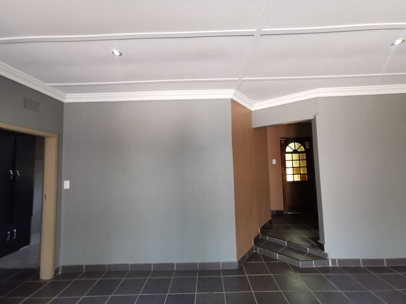 An empty living area featuring dark tiled flooring, recessed downlighting, and a coved ceiling, leading to a timber entrance door.