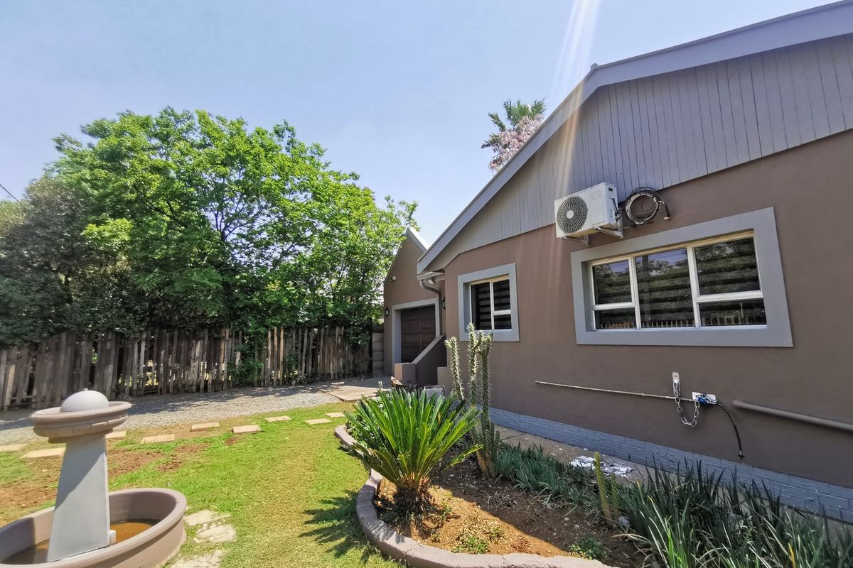 Rear exterior view of the house featuring a landscaped garden, a decorative fountain, and a paved driveway area.